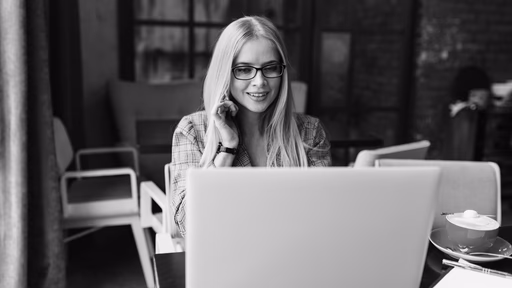 A woman talking on the phone while looking at a laptop.