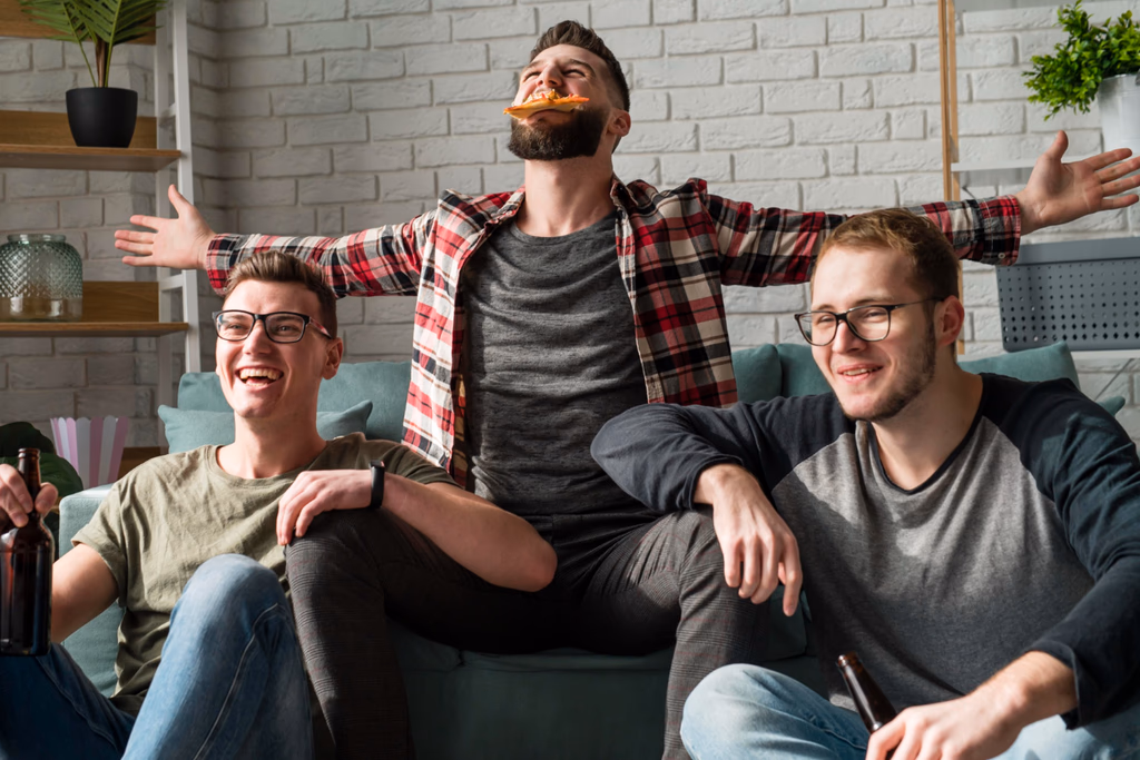 Friends relaxing on a couch while one balances a slice of pizza near his mouth.