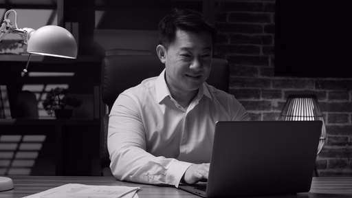 A man working at a laptop under a desk lamp.