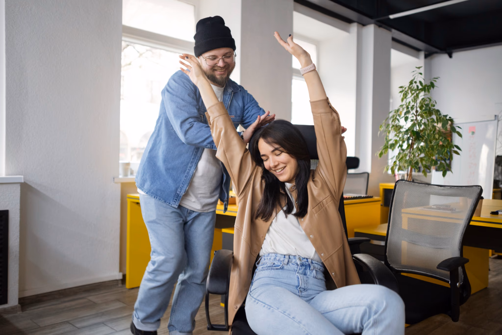 A seated coworker raising her arms while a colleague smiles beside her.