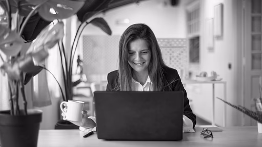 A woman holding a coffee cup while looking at her laptop.