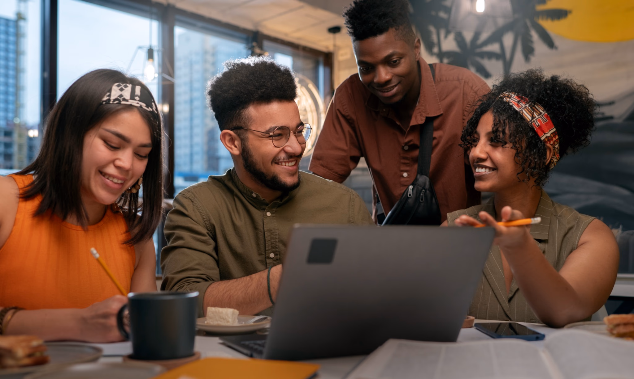 Four people gathered around a laptop at a shared table.