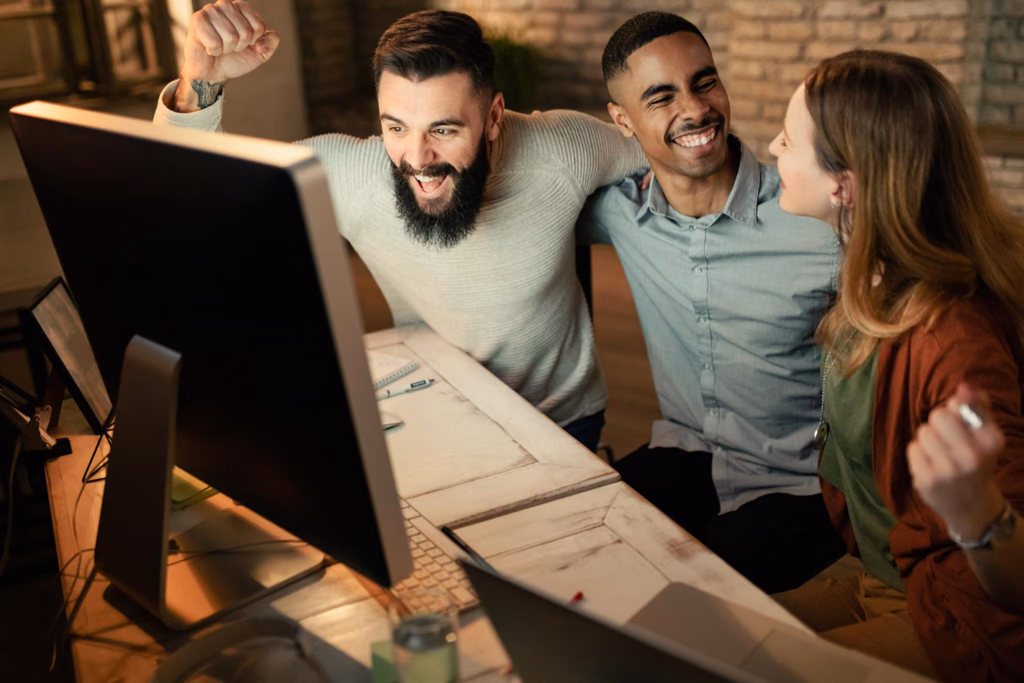 Three people smiling together in front of a desktop monitor.